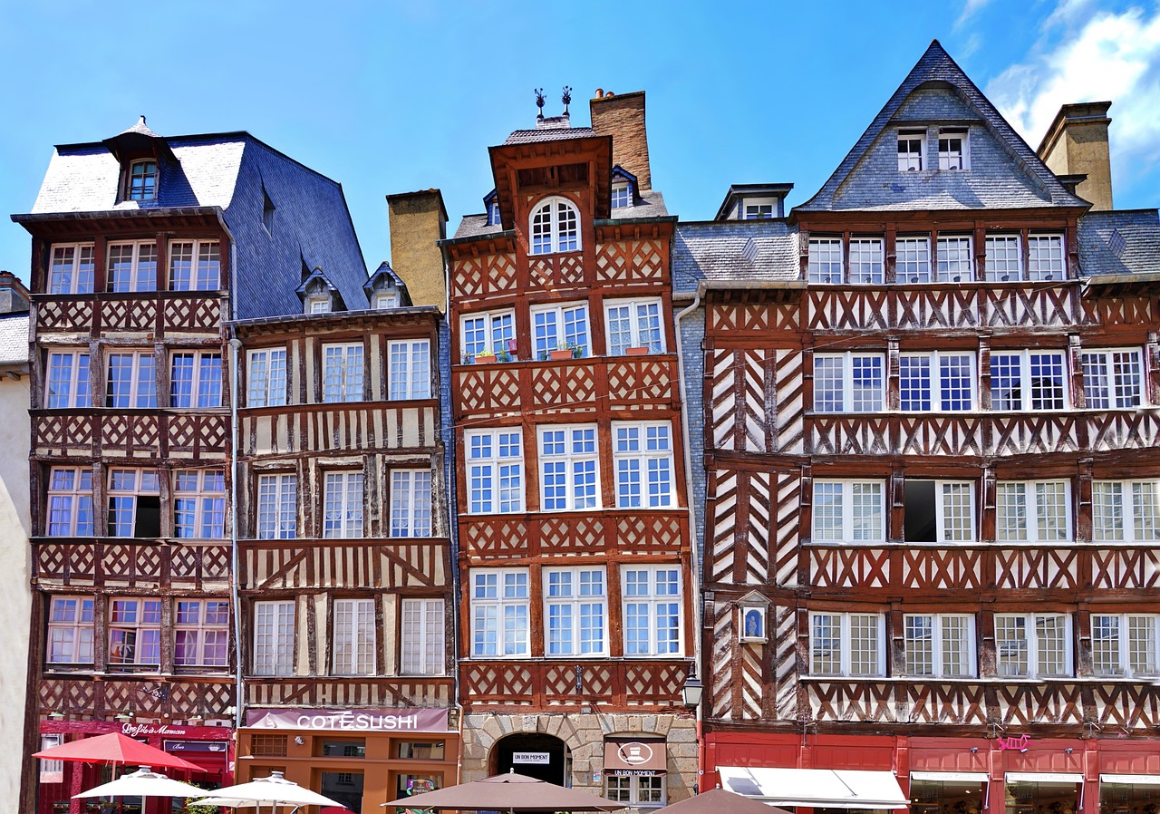 Sous un ciel bleu, ensemble d’immeubles penchés et colorés à pans de bois situés sur la place Champ Jaquet à Rennes.